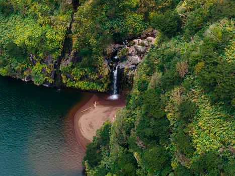 Aerial view of Caldeira Funda waterfall cascading into a volcanic lake surrounded by lush green cliffs and dense vegetation in Lajes das Flores Azores Portugal. Aerial view of Caldeira Funda waterfall cascading into a volcanic lake surrounded by lush green cliffs and dense vegetation in Lajes das Flores Azores Portugal.