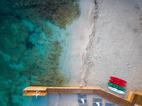 Aerial view of turquoise sea water sandy beach and colorful kayaks parked near a wooden pier in Ksamil Vlore County Albania. Aerial view of turquoise sea water sandy beach and colorful kayaks parked near a wooden pier in Ksamil Vlore County Albania.