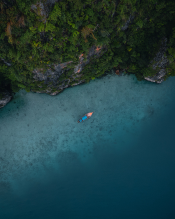 Aerial view of Pi Leh Bay featuring a traditional long tail boat floating on clear turquoise water near lush limestone cliffs Tambon Ao Nang Chang Wat Krabi Thailand. Aerial view of Pi Leh Bay featuring a traditional long tail boat floating on clear turquoise water near lush limestone cliffs Tambon Ao Nang Chang Wat Krabi Thailand.