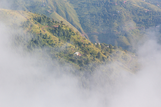 View of fog rolling across the lush green mountainside partially obscuring a small building nestled among the trees Pir Chanasi Azad Kashmir Pakistan. View of fog rolling across the lush green mountainside partially obscuring a small building nestled among the trees Pir Chanasi Azad Kashmir Pakistan.