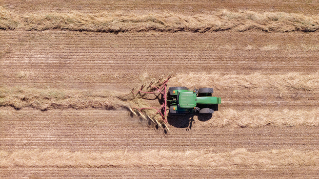 Aerial view of a green tractor pulling a hay rake through a dry harvested field in Philadelphia Western Cape South Africa. Aerial view of a green tractor pulling a hay rake through a dry harvested field in Philadelphia Western Cape South Africa.