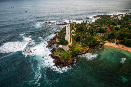 Aerial view of Dondra Lighthouse situated on a rocky headland surrounded by lush palm trees turquoise waters and crashing waves in Dondra Southern Province Sri Lanka. Aerial view of Dondra Lighthouse situated on a rocky headland surrounded by lush palm trees turquoise waters and crashing waves in Dondra Southern Province Sri Lanka.