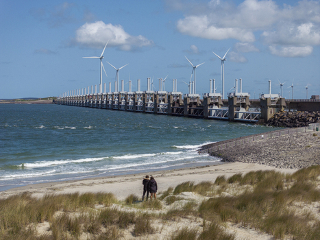 Aerial view of the Eastern Scheldt Storm Surge Barrier with wind turbines calm sea and sandy beach with two people standing on the dunes in Vrouwenpolder Zeeland Netherlands. Aerial view of the Eastern Scheldt Storm Surge Barrier with wind turbines calm sea and sandy beach with two people standing on the dunes in Vrouwenpolder Zeeland Netherlands.