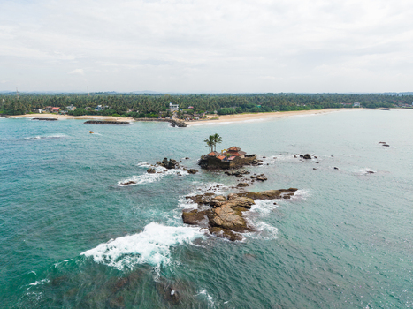 Aerial view of Seenigama Muhudu Dewalaya temple situated on a rocky island surrounded by turquoise ocean waves and a lush coastline in Peraliya Sri Lanka. Aerial view of Seenigama Muhudu Dewalaya temple situated on a rocky island surrounded by turquoise ocean waves and a lush coastline in Peraliya Sri Lanka.