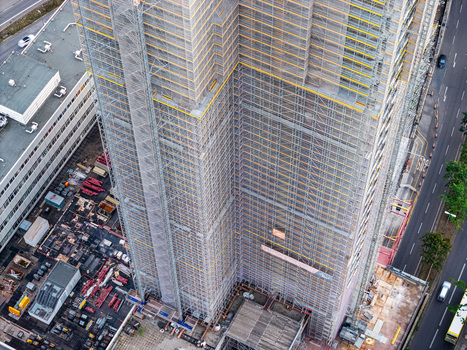 Aerial view of the Steglitzer Kreisel skyscraper under renovation covered in scaffolding and protective mesh with construction equipment on the ground in Berlin Berlin Germany. Aerial view of the Steglitzer Kreisel skyscraper under renovation covered in scaffolding and protective mesh with construction equipment on the ground in Berlin Berlin Germany.