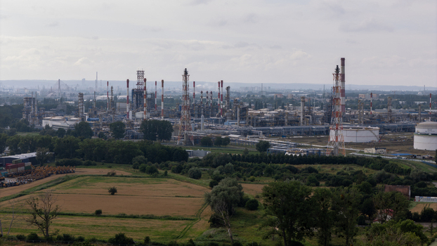 Aerial view of the industrial refinery complex featuring tall chimneys storage tanks and intricate pipe networks surrounded by green fields in Gdansk Pomeranian Voivodeship Poland. Aerial view of the industrial refinery complex featuring tall chimneys storage tanks and intricate pipe networks surrounded by green fields in Gdansk Pomeranian Voivodeship Poland.