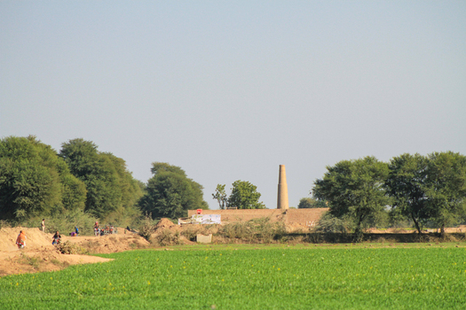View of the Cholistan Desert landscape featuring a brick kiln chimney lush green fields and trees under a clear sky in Bahawalpur Punjab Pakistan. View of the Cholistan Desert landscape featuring a brick kiln chimney lush green fields and trees under a clear sky in Bahawalpur Punjab Pakistan.