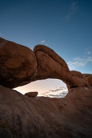 View of a natural rock archway framing a soft pastel sunset as it kisses the horizon creating a serene timeless landscape Spitzkoppe Erongo Region Namibia.