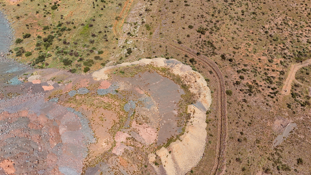 Aerial view of a landscape scarred by earthworks its layers of ochre rust and pale cream cutting through arid scrub revealing the raw textures of the land South Africa. Aerial view of a landscape scarred by earthworks its layers of ochre rust and pale cream cutting through arid scrub revealing the raw textures of the land South Africa.