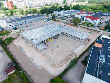 Aerial view of a large construction site featuring a steel frame structure for a new industrial building surrounded by paved lots and green areas in Riga Latvia. Aerial view of a large construction site featuring a steel frame structure for a new industrial building surrounded by paved lots and green areas in Riga Latvia.