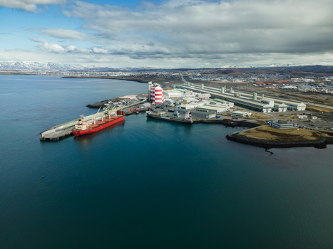 Hafnarfjordur Iceland 17 April 2026 Aerial view of the industrial port featuring a large red cargo ship docked near a red and white striped silo and extensive factory facilities under a cloudy sky. Hafnarfjordur Iceland 17 April 2026 Aerial view of the industrial port featuring a large red cargo ship docked near a red and white striped silo and extensive factory facilities under a cloudy sky.