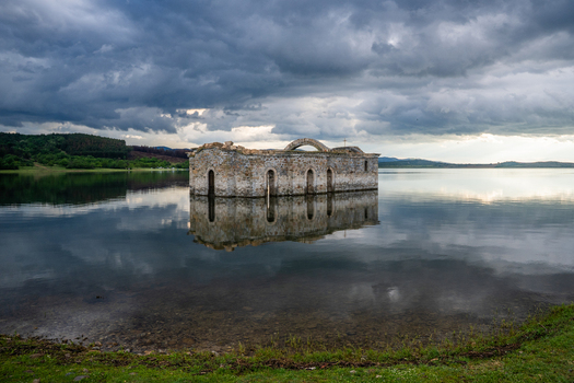 View of the submerged St. John of Rila church surrounded by calm water under a dramatic cloudy sky in Sliven Bulgaria. View of the submerged St. John of Rila church surrounded by calm water under a dramatic cloudy sky in Sliven Bulgaria.