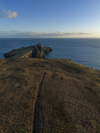 Aerial view of Neist Point Lighthouse situated on a dramatic rocky peninsula with steep cliffs and grassy headlands overlooking the blue sea Isle of Skye Scotland United Kingdom. Aerial view of Neist Point Lighthouse situated on a dramatic rocky peninsula with steep cliffs and grassy headlands overlooking the blue sea Isle of Skye Scotland United Kingdom.
