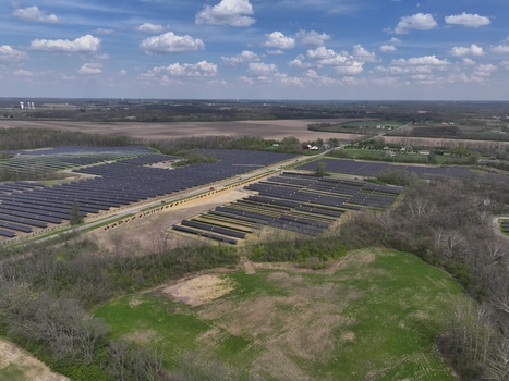 Lebanon United States 12 April 2026 Aerial view of a large solar farm with rows of panels surrounded by rural fields and trees under a cloudy blue sky.
