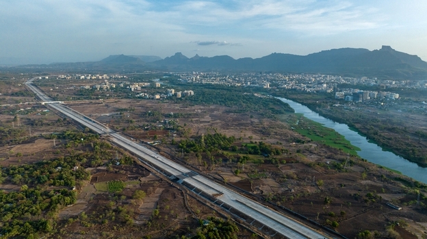 Aerial view of the JNPT highway infrastructure near Badlapur featuring a winding river surrounding plains and distant mountains in Badlapur Maharashtra India. Aerial view of the JNPT highway infrastructure near Badlapur featuring a winding river surrounding plains and distant mountains in Badlapur Maharashtra India.