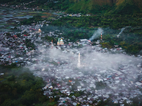 Aerial view of the village of Sembalun nestled in an agricultural basin at the foothills of Mount Rinjani with mist drifting over rooftops and mosques in Sembalun West Nusa Tenggara Indonesia. Aerial view of the village of Sembalun nestled in an agricultural basin at the foothills of Mount Rinjani with mist drifting over rooftops and mosques in Sembalun West Nusa Tenggara Indonesia.