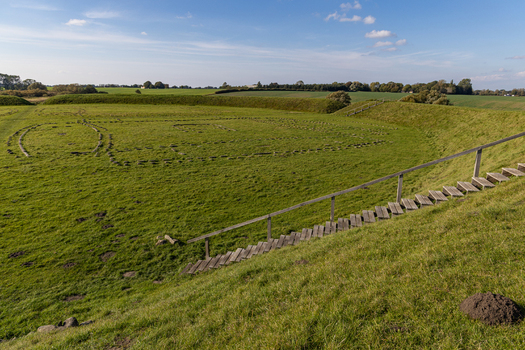 View of The Viking Fortress Trelleborg showing the circular earthen ramparts and stone outlines of longhouses on a grassy field under a clear blue sky in Slagelse Sjaeland Denmark. View of The Viking Fortress Trelleborg showing the circular earthen ramparts and stone outlines of longhouses on a grassy field under a clear blue sky in Slagelse Sjaeland Denmark.