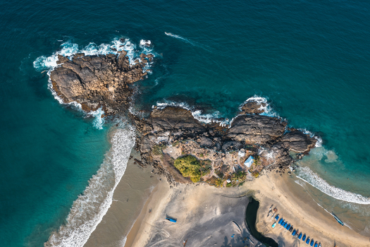 Aerial view of a rocky peninsula and sandy beach with turquoise ocean waves and small blue boats lined up on the shore in Kovalam Kerala India. Aerial view of a rocky peninsula and sandy beach with turquoise ocean waves and small blue boats lined up on the shore in Kovalam Kerala India.