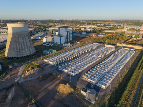 Aerial view of the Cargovil battery energy storage system with rows of white energy storage units and a large cooling tower in an industrial landscape in Vilvoorde Vlaanderen Belgium. Aerial view of the Cargovil battery energy storage system with rows of white energy storage units and a large cooling tower in an industrial landscape in Vilvoorde Vlaanderen Belgium.