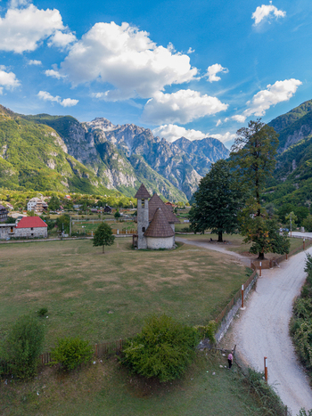 Aerial view of the historic Church of Theth nestled in a green valley surrounded by the dramatic peaks of the Accursed Mountains in Theth Shkoder County Albania. Aerial view of the historic Church of Theth nestled in a green valley surrounded by the dramatic peaks of the Accursed Mountains in Theth Shkoder County Albania.