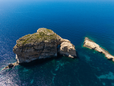 Aerial view of Fungus Rock in Dwejra Bay surrounded by the deep blue Mediterranean Sea and rocky coastline in Gozo Region Malta. Aerial view of Fungus Rock in Dwejra Bay surrounded by the deep blue Mediterranean Sea and rocky coastline in Gozo Region Malta.