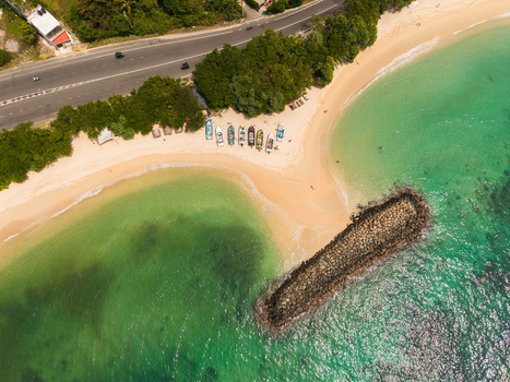 Aerial view of Devil s Rock and a sandy beach with colorful fishing boats turquoise ocean water a coastal road and lush tropical trees Ahangama Southern Province Sri Lanka. Aerial view of Devil s Rock and a sandy beach with colorful fishing boats turquoise ocean water a coastal road and lush tropical trees Ahangama Southern Province Sri Lanka.