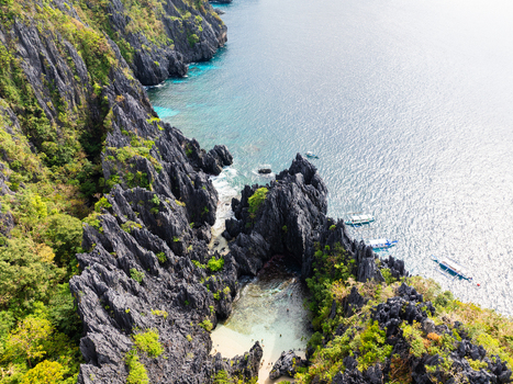 Aerial view of Secret Beach surrounded by jagged limestone cliffs and turquoise waters with boats anchored nearby in El Nido Mimaropa Philippines.
