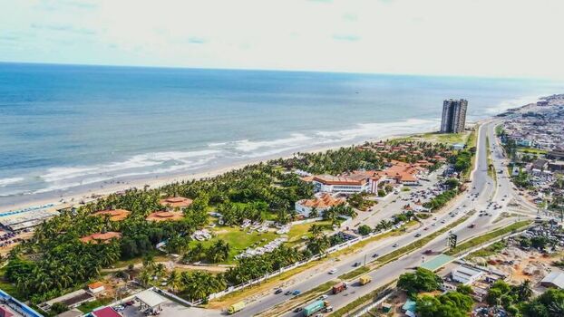 Aerial view of a coastal resort featuring lush palm trees low rise buildings and a nearby highway stretching along the sandy beach in Ghana. Aerial view of a coastal resort featuring lush palm trees low rise buildings and a nearby highway stretching along the sandy beach in Ghana.
