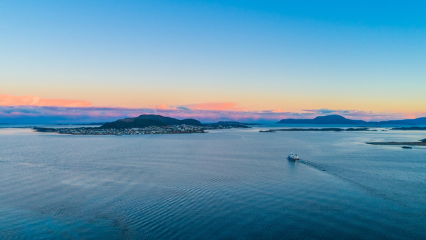 Aerial view of the coastal town with a boat sailing in the calm sea under a vibrant sunset sky in Alesund More og Romsdal Norway. Aerial view of the coastal town with a boat sailing in the calm sea under a vibrant sunset sky in Alesund More og Romsdal Norway.