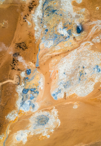 Aerial view of Hverir geothermal area featuring steaming vents boiling mud pools and colorful mineral deposits with tourists walking on paths Reykjahlid THingeyjarsveit Iceland.