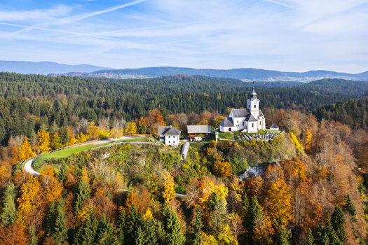 Aerial view of a striking white church perched atop a hill amidst the vibrant autumn colors of the forest Sternberg Kärnten Austria. Aerial view of a striking white church perched atop a hill amidst the vibrant autumn colors of the forest Sternberg Kärnten Austria.