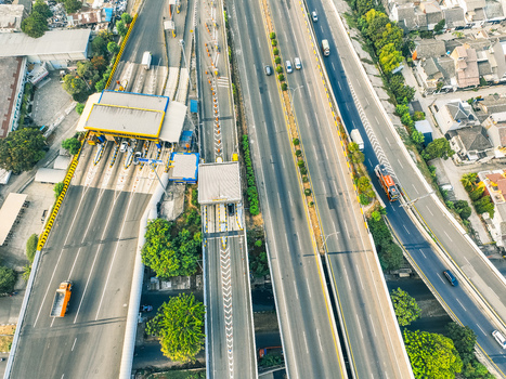 Aerial view of Cikunir toll gate with vehicles passing through lanes surrounded by urban infrastructure trees and residential buildings in Kecamatan Bekasi Selatan Jawa Barat Indonesia. Aerial view of Cikunir toll gate with vehicles passing through lanes surrounded by urban infrastructure trees and residential buildings in Kecamatan Bekasi Selatan Jawa Barat Indonesia.