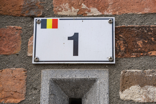 View of a house number plate with the number one and a small Belgian flag mounted on a rustic brick wall in Baarle Hertog Flanders Belgium.