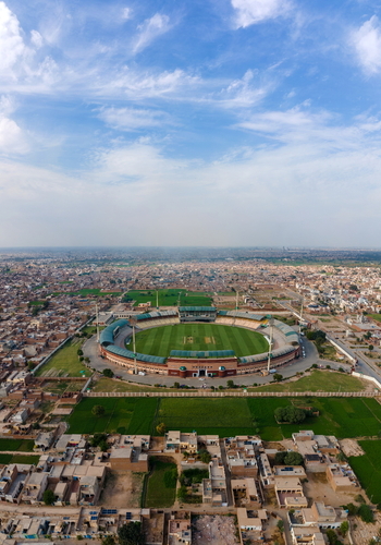 Aerial view of Multan International Cricket Stadium surrounded by urban sprawl green fields and clear blue sky in Multan Punjab Pakistan.