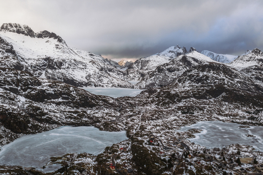 Aerial view of snow dusted peaks and frozen lakes under a dramatic sky create a serene yet rugged landscape Tind Nordland Norway.