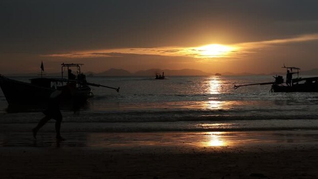 View of longtail boats and a person at sunset Thailand.