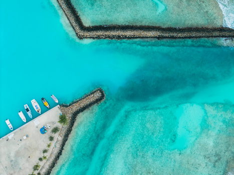 Aerial view of boats moored at the pier contrasting with the vibrant turquoise waters and dark breakwaters creating a striking visual harmony Vashafaru Island Maldives. Aerial view of boats moored at the pier contrasting with the vibrant turquoise waters and dark breakwaters creating a striking visual harmony Vashafaru Island Maldives.