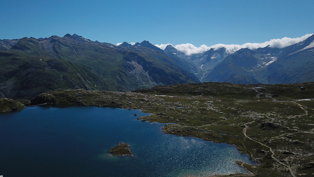 Aerial view of Grimsel Pass featuring the Totensee lake surrounded by rugged alpine terrain and distant mountain peaks under a clear blue sky Obergoms Valais Switzerland. Aerial view of Grimsel Pass featuring the Totensee lake surrounded by rugged alpine terrain and distant mountain peaks under a clear blue sky Obergoms Valais Switzerland.