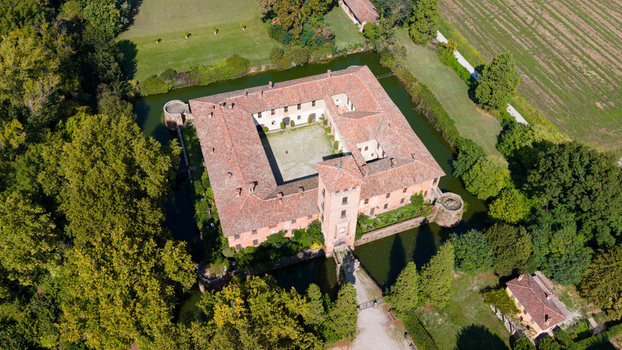 Aerial view of Castello di Peschiera Borromeo with its historic moat lush green trees and surrounding agricultural fields in Peschiera Borromeo Lombardy Italy.