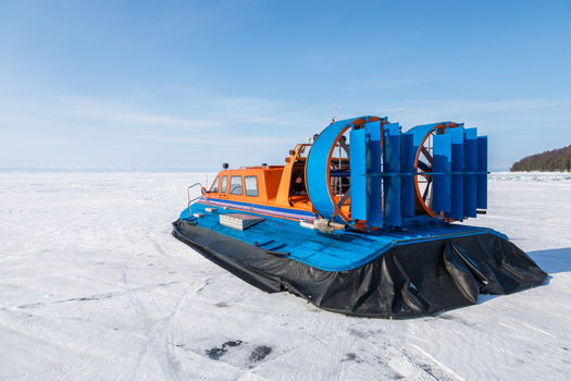 View of an orange and blue hovercraft resting on the vast frozen surface of Lake Baikal under a clear blue sky in Severobaykalsk Buryatia Russia. View of an orange and blue hovercraft resting on the vast frozen surface of Lake Baikal under a clear blue sky in Severobaykalsk Buryatia Russia.