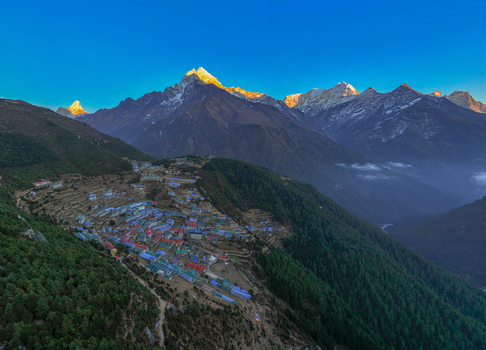 Aerial view of Namche Bazaar nestled in the Himalayas featuring colorful rooftops terraced hillsides pine forests and snow capped peaks illuminated by golden hour light in Nepal.
