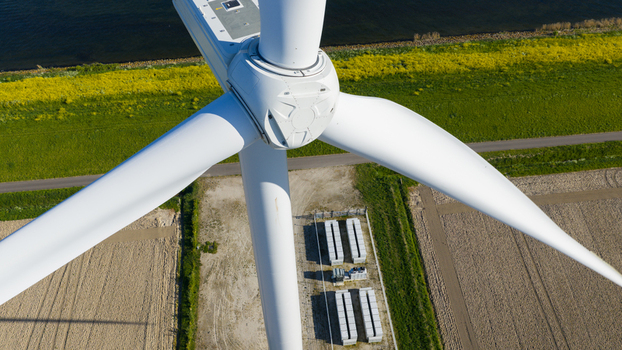 Aerial view of a wind turbine nacelle and blades with battery storage units on the ground near green fields and agricultural land Ooltgensplaat South Holland Netherlands. Aerial view of a wind turbine nacelle and blades with battery storage units on the ground near green fields and agricultural land Ooltgensplaat South Holland Netherlands.