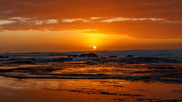 Aerial view of Hartenbos beach with waves crashing against rocks under a vibrant orange sunset sky in Mossel Bay Western Cape South Africa. Aerial view of Hartenbos beach with waves crashing against rocks under a vibrant orange sunset sky in Mossel Bay Western Cape South Africa.