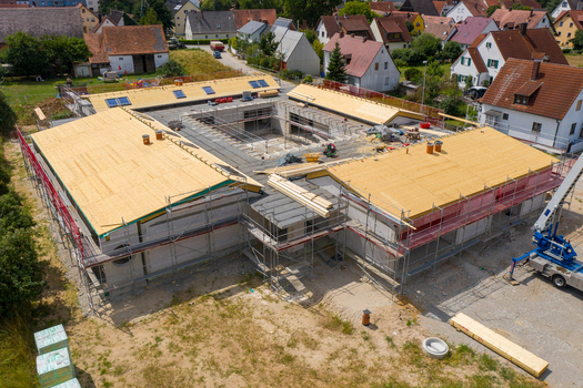 Igensdorf Germany 11 May 2024 Aerial view of a modern building under construction with a large wooden roof structure and scaffolding in a residential area. Igensdorf Germany 11 May 2024 Aerial view of a modern building under construction with a large wooden roof structure and scaffolding in a residential area.