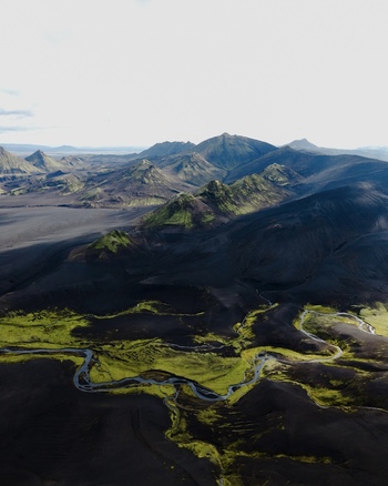 Aerial view of winding river snaking through volcanic black sands contrasting vividly with patches of bright green moss Landmannalaugar Iceland. Aerial view of winding river snaking through volcanic black sands contrasting vividly with patches of bright green moss Landmannalaugar Iceland.
