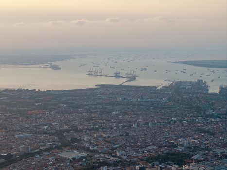 Aerial view of the port of Surabaya with industrial cranes and numerous ships in the bay overlooking the dense urban sprawl of the city in Surabaya East Java Indonesia. Aerial view of the port of Surabaya with industrial cranes and numerous ships in the bay overlooking the dense urban sprawl of the city in Surabaya East Java Indonesia.