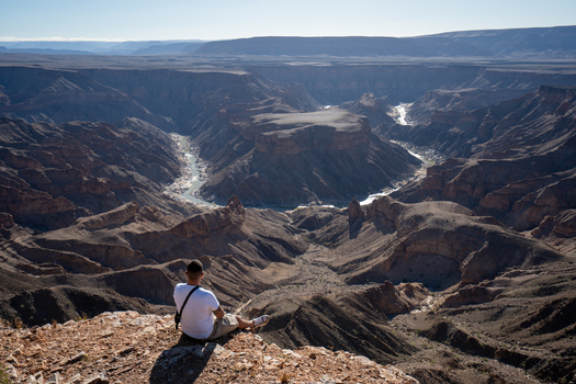 View of a lone figure perched on the precipice gazing into the shadowed depths of a vast canyon carved by a winding river Keetmanshoop Namibia. View of a lone figure perched on the precipice gazing into the shadowed depths of a vast canyon carved by a winding river Keetmanshoop Namibia.