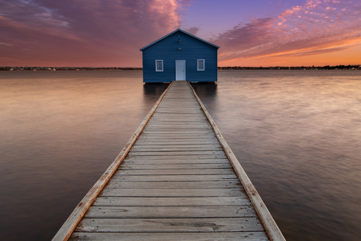View of the iconic Blue Boat House at the end of a long wooden jetty over the calm waters of the Swan River during a vibrant sunset in Crawley Western Australia Australia. View of the iconic Blue Boat House at the end of a long wooden jetty over the calm waters of the Swan River during a vibrant sunset in Crawley Western Australia Australia.