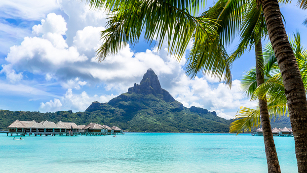 View of Mount Otemanu rising above the turquoise lagoon and overwater bungalows with palm trees in the foreground in Bora Bora Leeward Islands French Polynesia.