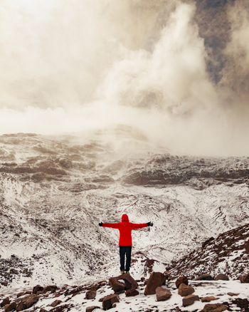 Aerial view of a person in a bright red jacket standing with arms outstretched on the snowy rocky slopes of Volcano Chimborazo in Guano Chimborazo Ecuador. Aerial view of a person in a bright red jacket standing with arms outstretched on the snowy rocky slopes of Volcano Chimborazo in Guano Chimborazo Ecuador.